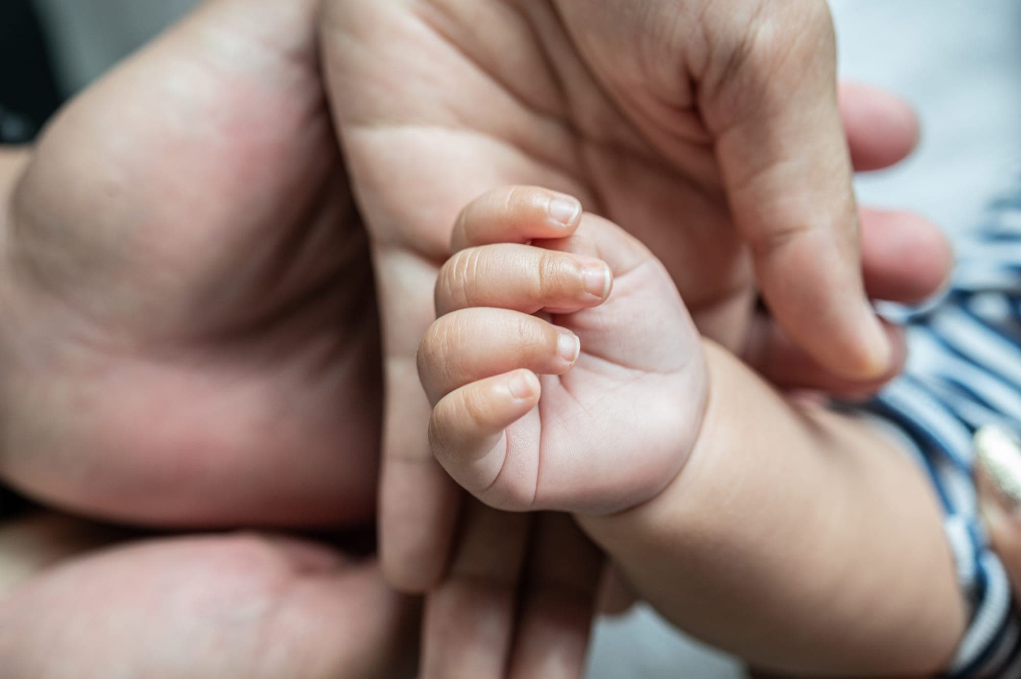 Main d’adulte tenant les pieds d’un bébé, accompagnement au quotidien après la naissance