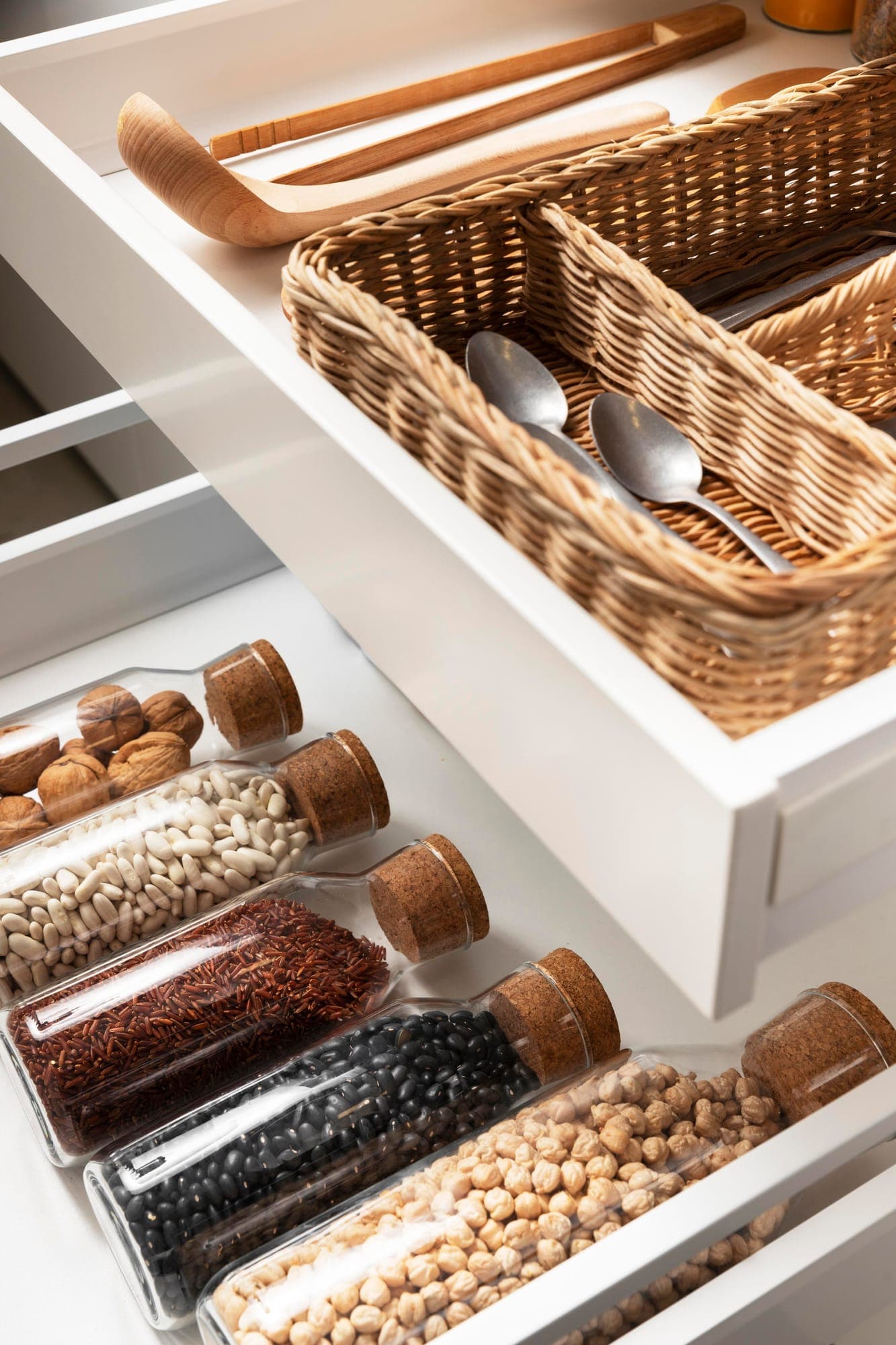 Tiroir de cuisine organisé avec bocaux de légumineuses et couverts après un rangement